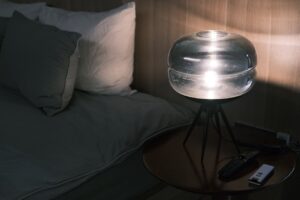 A small bedside lamp lit on a nightstand beside made-up bedding