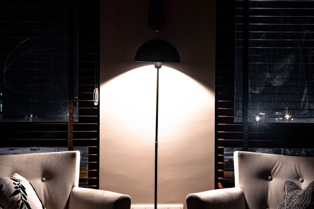 A floor lamp lighting two armchairs in a dark living room at night