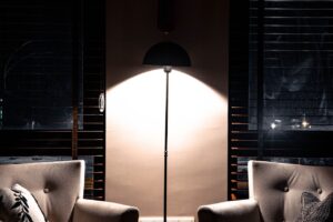 A floor lamp lighting two armchairs in a dark living room at night